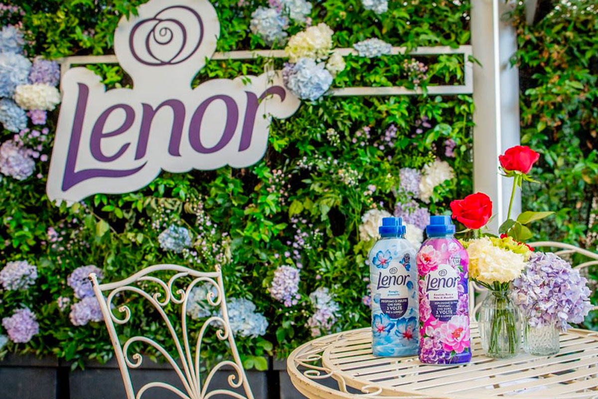 Flaconi di ammorbidente Lenor con bolle di profumo 2.0 su un tavolino da giardino decorato con fiori e rose.