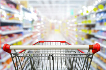 Carrello della spesa vuoto in un supermercato, vista in prima persona tra gli scaffali del largo consumo.