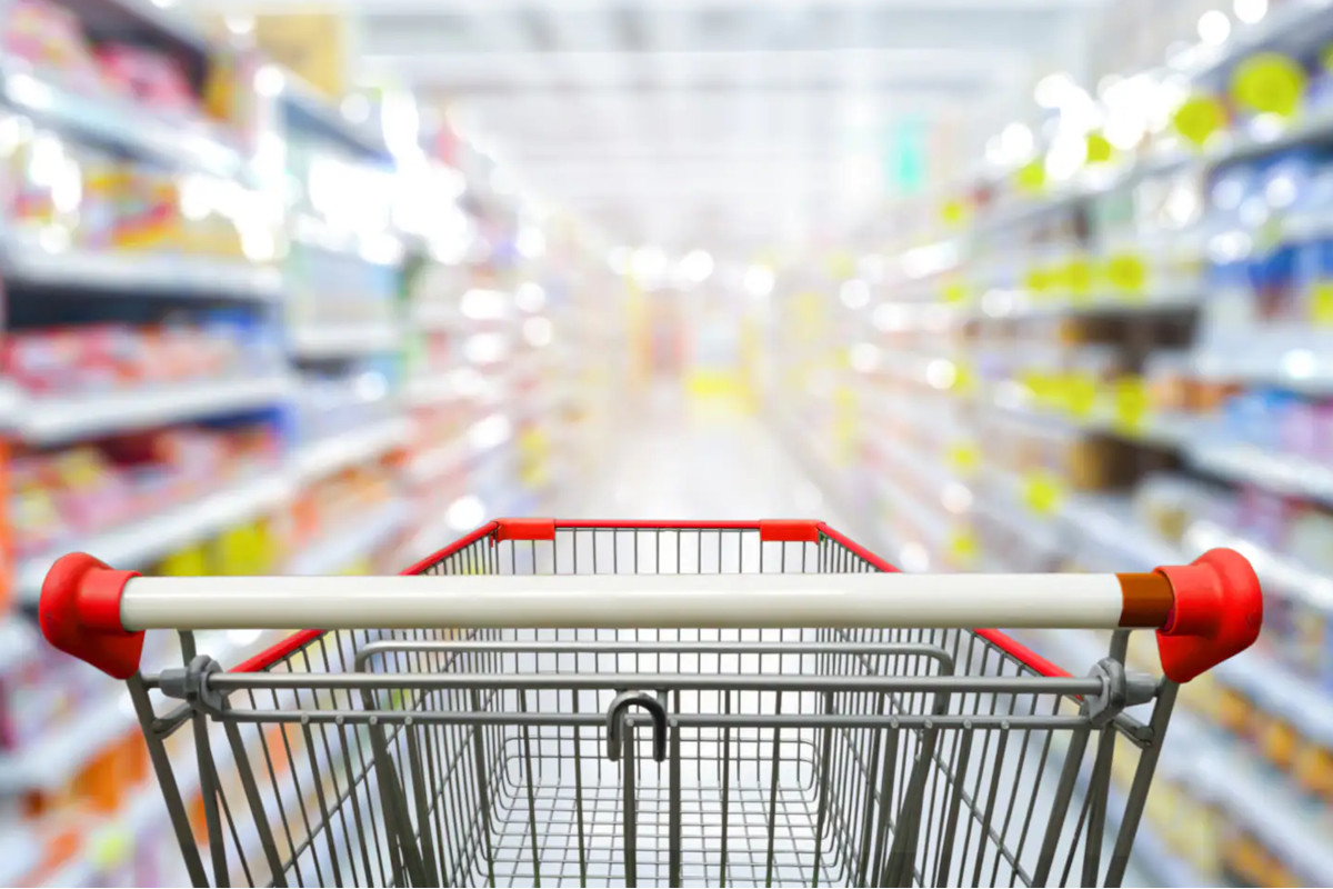 Carrello della spesa vuoto in un supermercato, vista in prima persona tra gli scaffali del largo consumo.
