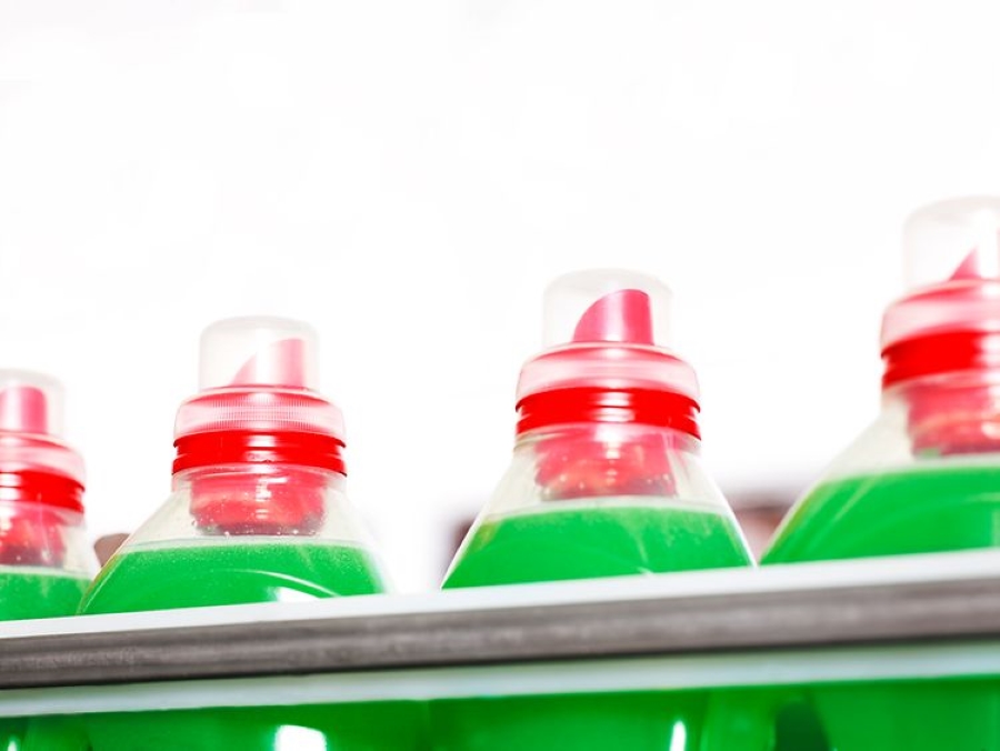 Flaconi di detersivo Henkel Home Care con tappo rosso e liquido verde su scaffale, prodotti per la pulizia della casa.