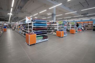 Supermercato con corsie ampie, scaffali pieni di prodotti e display arancioni per il repertorio 2025.