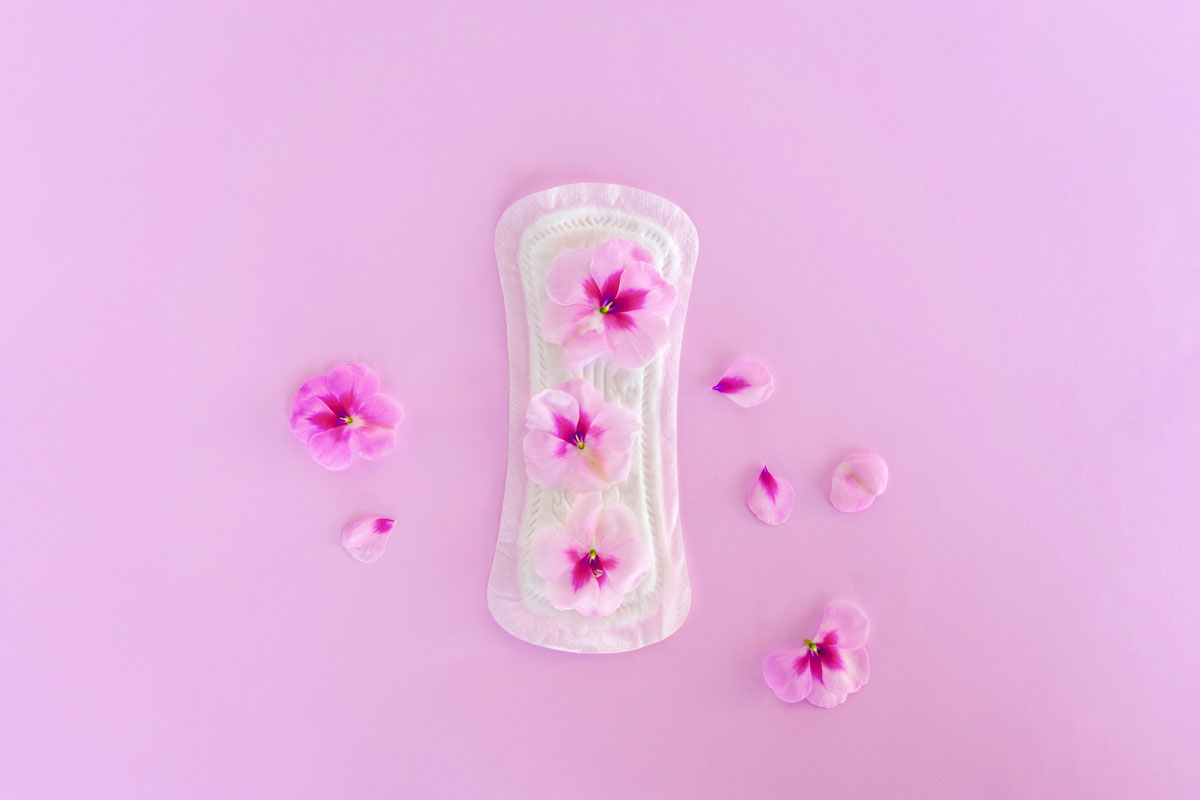 Assorbenza femminile su sfondo rosa con fiori. Assorbenti green e naturali per l'igiene intima.