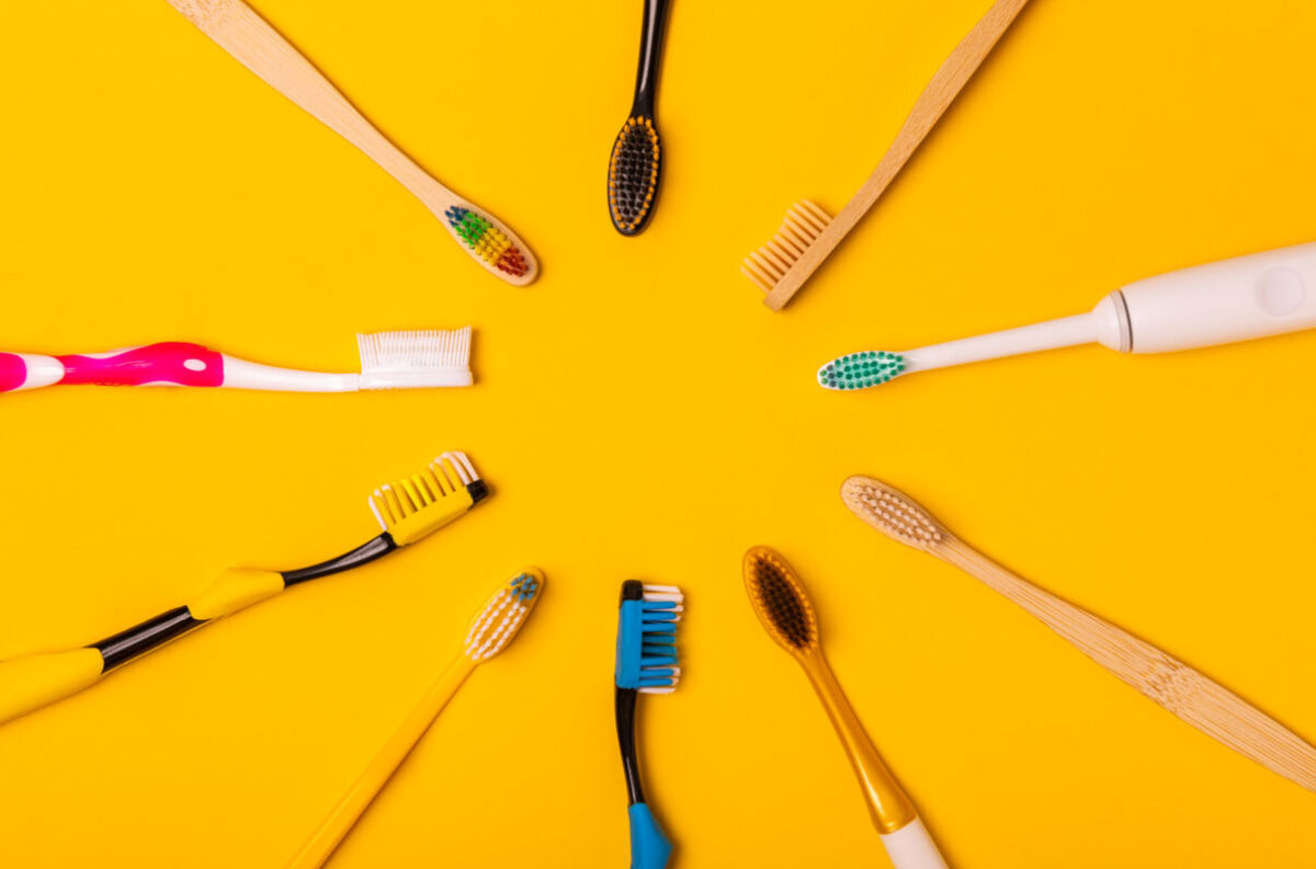 Spazzolini da denti: manuali, elettrici e in bambù su sfondo giallo. Igiene orale e cura dentale.
