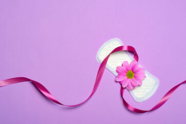 Assorbente femminile su sfondo lilla con fiore rosa e nastro. Igiene intima e cura femminile.