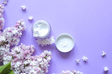 Creme corpo e fiori lilla su sfondo viola. Bodycare e bellezza.