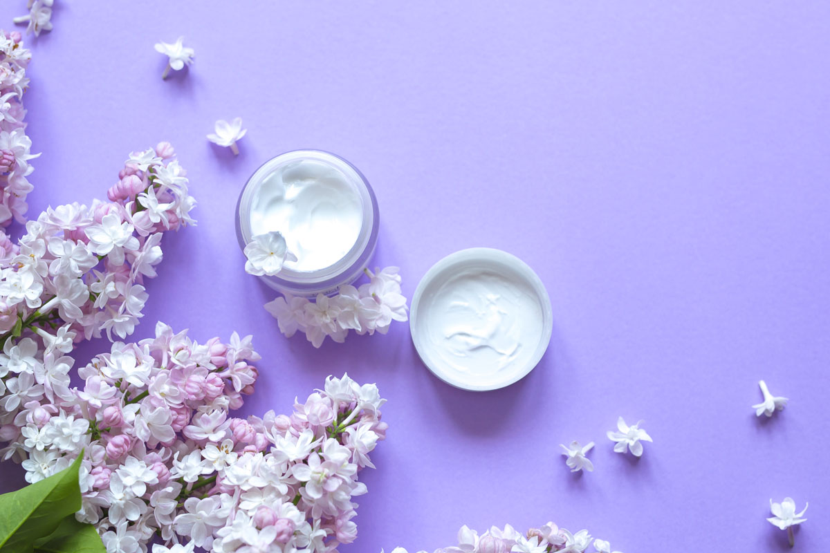 Creme corpo e fiori lilla su sfondo viola. Bodycare e bellezza.