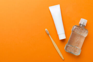 Igiene orale: spazzolino, dentifricio e collutorio su sfondo arancione. Cura dentale quotidiana.