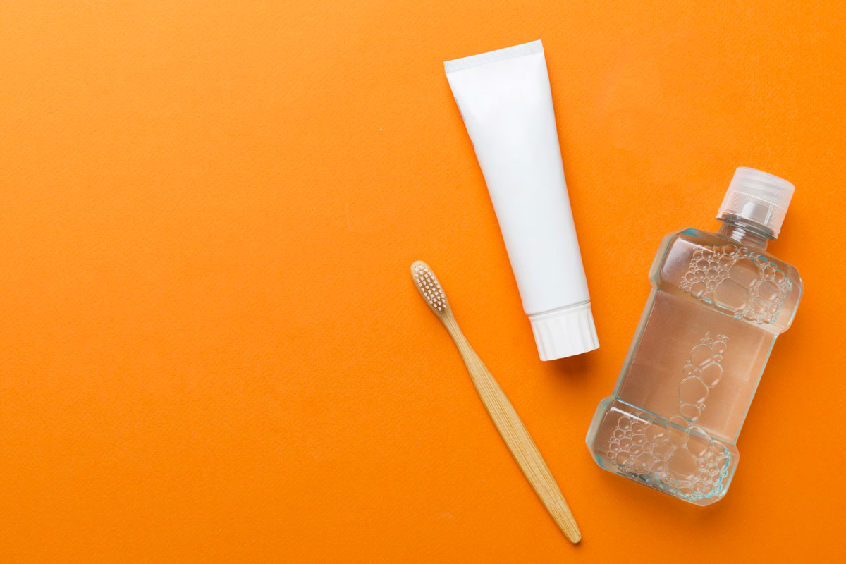 Igiene orale: spazzolino, dentifricio e collutorio su sfondo arancione. Cura dentale quotidiana.