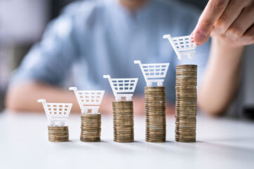 Inflazione: Carrelli spesa su pile di monete. Aumento prezzi e costo della vita.