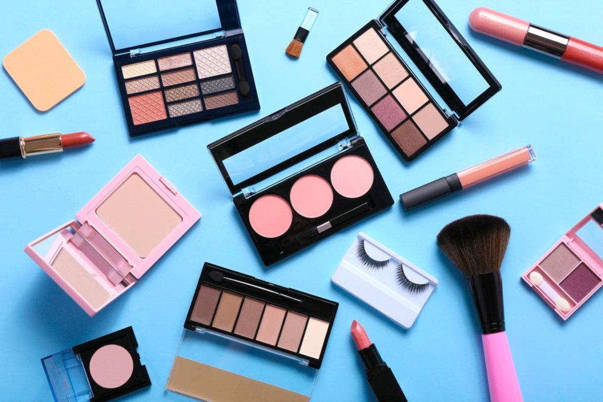 Make-up: palette ombretti, rossetti, blush e pennelli su sfondo azzurro. Tendenze beauty 2025.