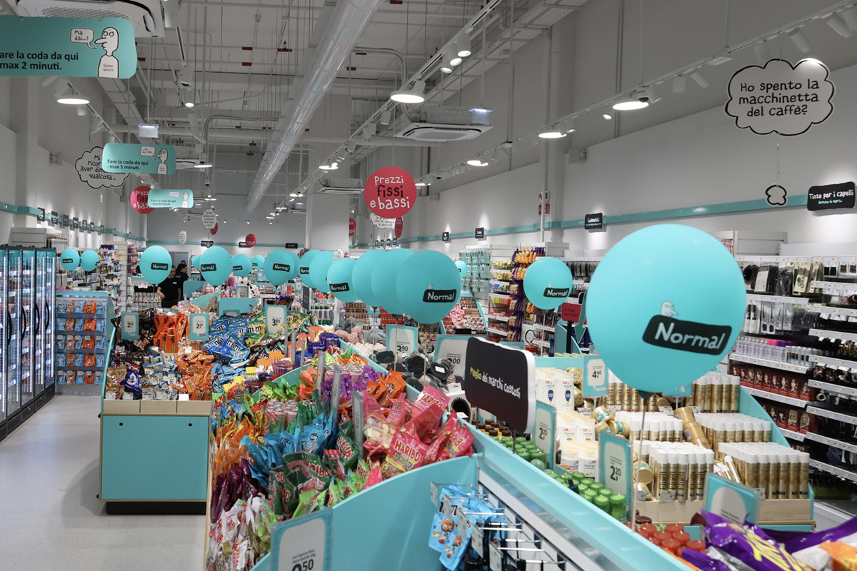 Interno negozio Normal Arese. Scaffali pieni di prodotti, palloncini azzurri. Nuova apertura Normal, prezzi fissi e bassi.