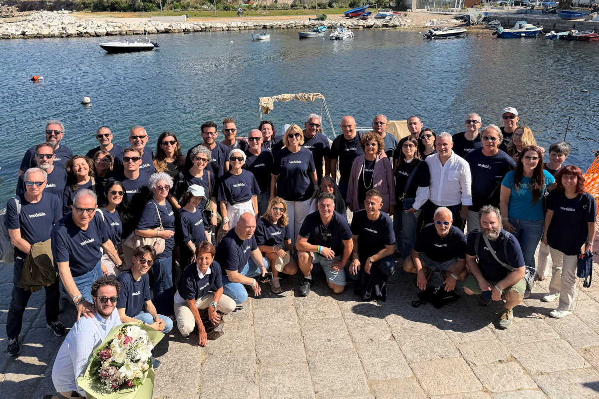 Gruppo di persone in maglietta blu alla Convention Coralis 2026 posa per una foto ricordo davanti al porto turistico.