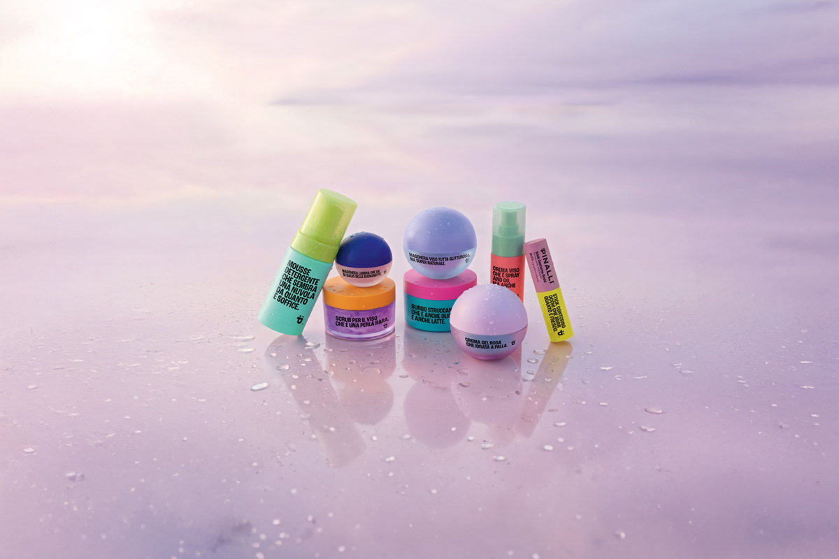 Linea skincare Pinalli: flaconi, barattoli e prodotti viso colorati disposti su una superficie bagnata color pastello.