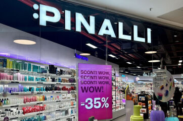 Insegna luminosa del negozio Pinalli in Lombardia con scaffali di prodotti di bellezza e cartello promozionale al -35%.