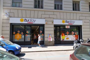 Facciata esterna del punto vendita Tuday Conad con insegna, vetrine decorate e clienti all'ingresso in città.