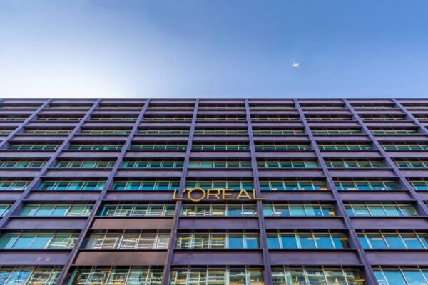 Facciata moderna della sede L'Oréal con logo aziendale dorato e cielo azzurro sullo sfondo.