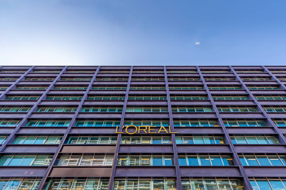Facciata moderna della sede L'Oréal con logo aziendale dorato e cielo azzurro sullo sfondo.