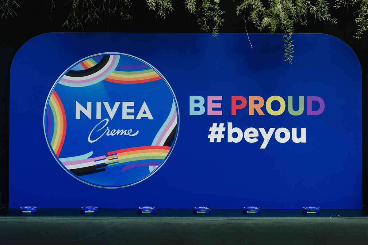 Pannello blu NIVEA Creme con logo arcobaleno, scritta BE PROUD e hashtag #beyou per la collaborazione con Arcigay.