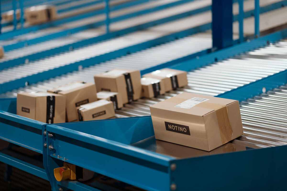 Pacchi con logo Notino su un nastro trasportatore automatizzato in un centro logistico per la spedizione degli ordini.