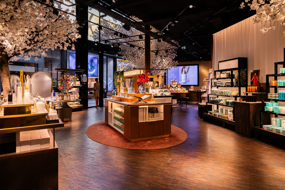 Interni di una boutique Rituals rinnovata con espositori di prodotti beauty, alberi di ciliegio e design elegante.