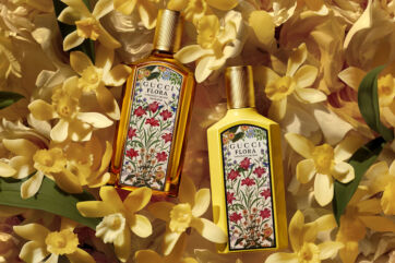 Due flaconi di profumo Gucci Flora Gorgeous Orchid su uno sfondo di fiori gialli, parte della collezione Gucci Beauty.