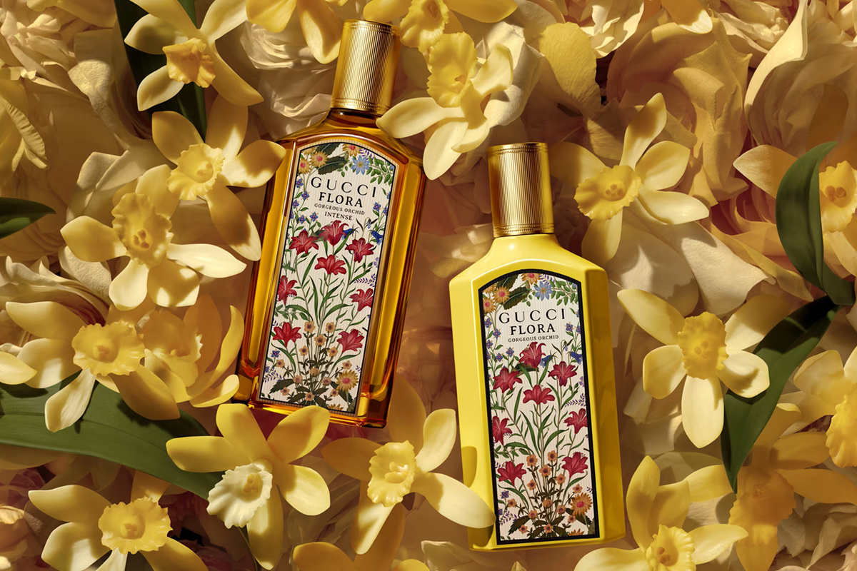 Due flaconi di profumo Gucci Flora Gorgeous Orchid su uno sfondo di fiori gialli, parte della collezione Gucci Beauty.
