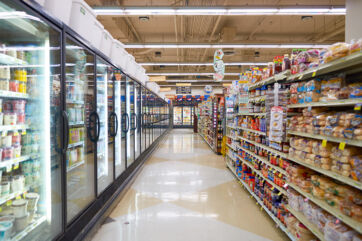 Corsia di un supermercato con scaffali di prodotti alimentari e lunghe vetrine refrigerate per il retail moderno.