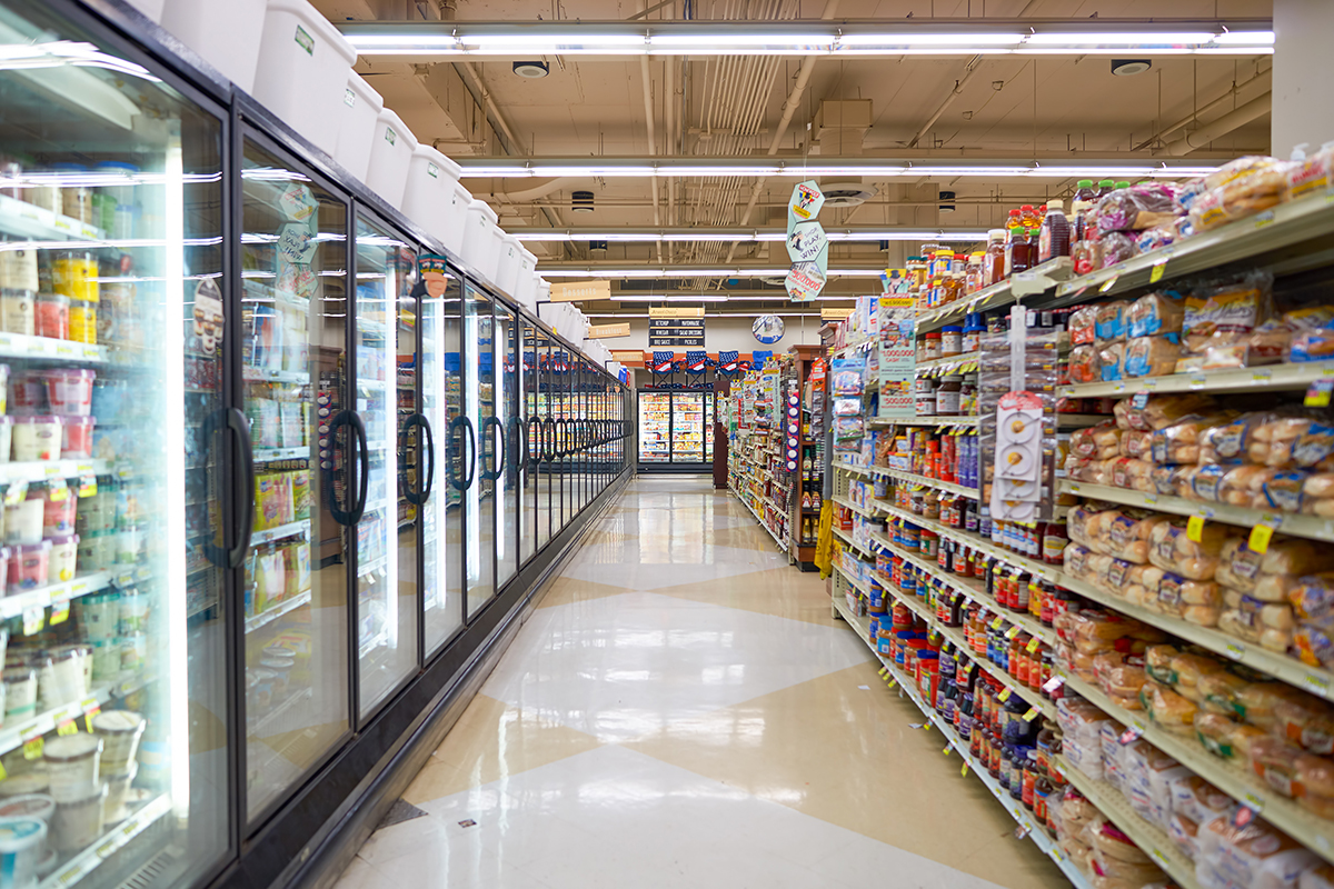Corsia di un supermercato con scaffali di prodotti alimentari e lunghe vetrine refrigerate per il retail moderno.