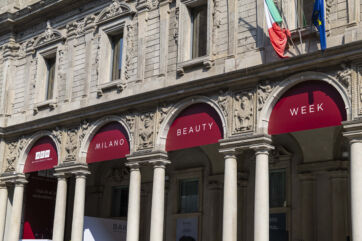 Facciata di Palazzo Giureconsulti a Milano con arcate e bandiere, allestita per la Milano Beauty Week 2025