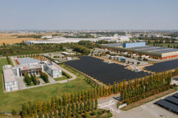 Veduta aerea di un grande parco fotovoltaico con pannelli solari, edifici industriali e aree verdi