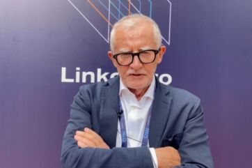 Mario Gasbarrino in giacca blu e camicia bianca, con occhiali, ritratto davanti a uno sfondo aziendale con logo Linkontro.