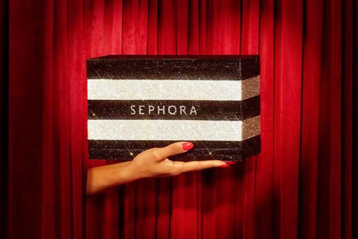 Mano che regge una scatola Sephora glitterata a righe su sfondo di tende rosse per il social commerce su TikTok.