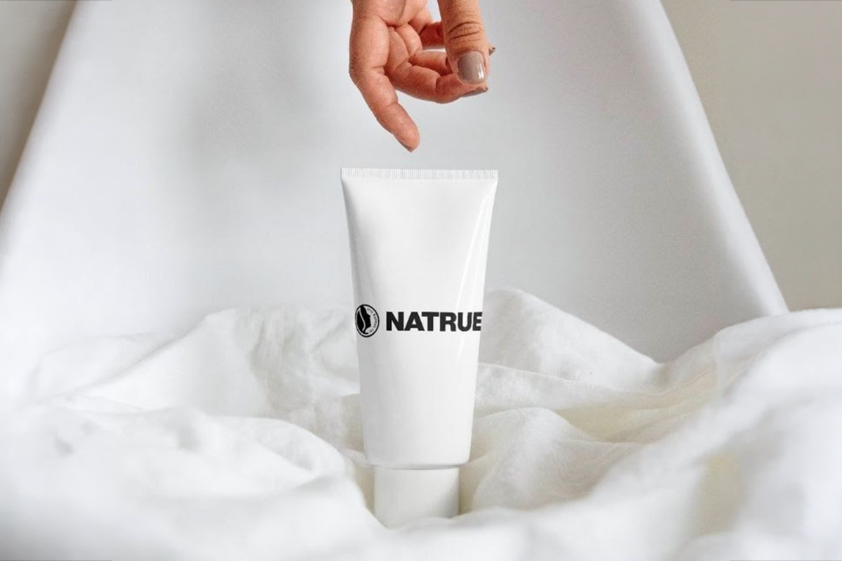 Mano tiene tubo bianco NATRUE su tessuto: beauty naturale certificato per cosmetici bio e sostenibili.