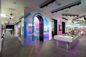 Interno del negozio Pinalli a Milano: arco luminoso beauty gallery, espositori cosmetici e area cassa.