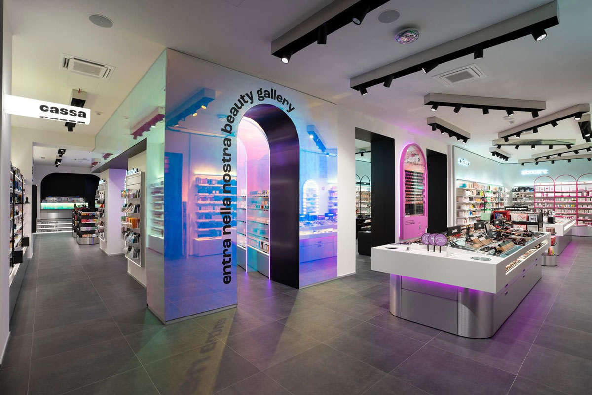 Interno del negozio Pinalli a Milano: arco luminoso beauty gallery, espositori cosmetici e area cassa.